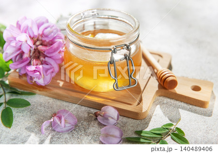 Acacia honey jar with blooming flowers and wooden dipper Acacia honey jar with blooming flowers and wooden dipper 140489406