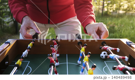 Person in a red jacket playing table football outdoors in a garden setting, capturing everyday joy and simple outdoor fun. 140489498