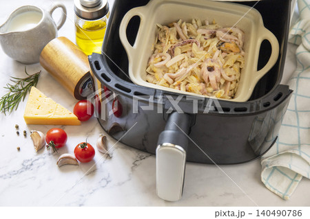 Pasta with seafood in creamy cheese sauce, in kitchen gadget modern white air fryer. Lifestyle trendy of new cooking. Copy space. 140490786
