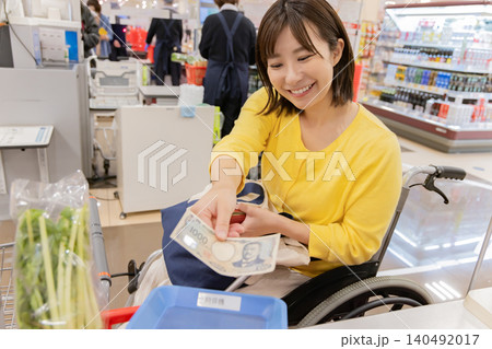 スーパーのレジで支払いをする車椅子の女性 スーパーのレジで支払いをする車椅子の女性 140492017