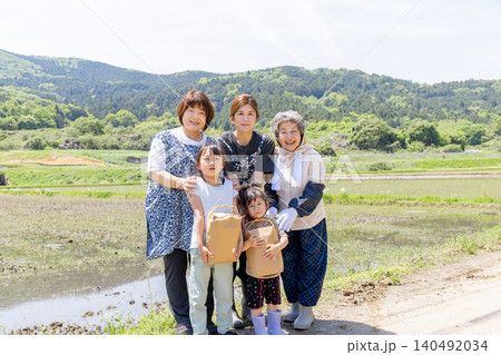里山の水田で収穫物を手に笑顔を見せる三世代の日本人女性と子供 140492034