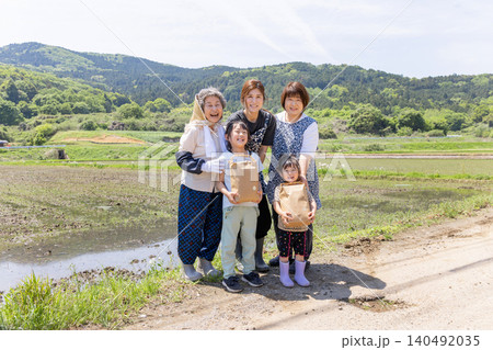 里山の水田で収穫物を手に笑顔を見せる三世代の日本人女性と子供 里山の水田で収穫物を手に笑顔を見せる三世代の日本人女性と子供 140492035