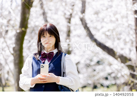 桜並木の下でスマートフォンを持つ女子高校生の春のポートレート 桜並木の下でスマートフォンを持つ女子高校生の春のポートレート 140492058