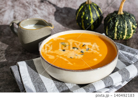 Bowl of creamy pumpkin soup topped with pumpkin seeds. Rich orange puree is served in rustic bowl and decorated with crunchy seeds creating an appetizing autumn meal presentation. Concept of seasonal Bowl of creamy pumpkin soup topped with pumpkin seeds. Rich orange puree is served in rustic bowl and decorated with crunchy seeds creating an appetizing autumn meal presentation. Concept of seasonal 140492183