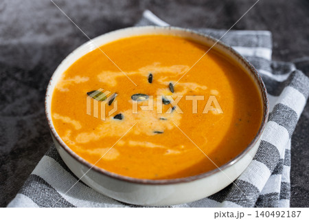 Bowl of creamy pumpkin soup topped with pumpkin seeds. Rich orange puree is served in rustic bowl and decorated with crunchy seeds creating an appetizing autumn meal presentation. Concept of seasonal Bowl of creamy pumpkin soup topped with pumpkin seeds. Rich orange puree is served in rustic bowl and decorated with crunchy seeds creating an appetizing autumn meal presentation. Concept of seasonal 140492187