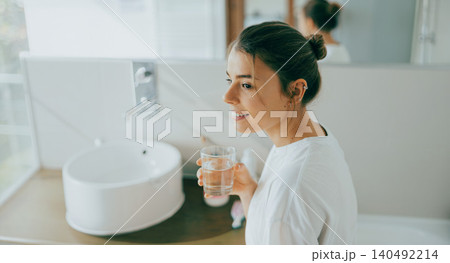 Happy young Caucasian woman holding a glass of water in a bright modern bathroom Happy young Caucasian woman holding a glass of water in a bright modern bathroom 140492214
