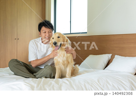ベッドの上でゴールデンレトリバーとふれあう男性 140492308
