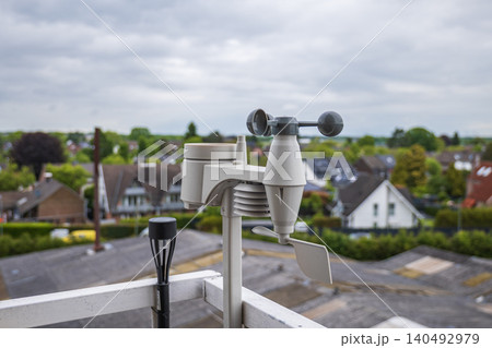 Home weather station anemometer on balcony railing measuring wind speed and direction with suburban background 140492979