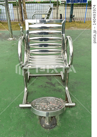 This seated exercise equipment, made of stainless steel, allows users to place their legs on a circle and rotate it back , in a public park. 140493974