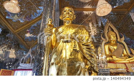 UTHAI THANI, THAILAND - MAY 2, 2025. A golden statue of a revered Buddhist monk (Luang Phor Ruesi Lingdam) sits inside the famous Mirrored Crystal Sanctuary (Prasat Thong Kham) at Wat Tha Sung temple  140494349
