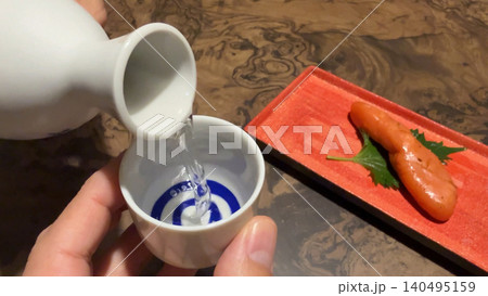 冷酒を酒器から注ぐ晩酌シーン 炙りたらこと楽しむ和食と日本酒 冷酒を酒器から注ぐ晩酌シーン 炙りたらこと楽しむ和食と日本酒 140495159
