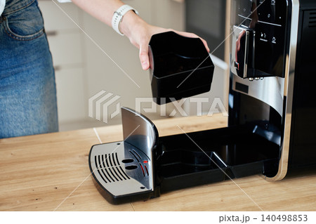 Woman holding coffee machine grounds container during cleaning Woman holding coffee machine grounds container during cleaning 140498853