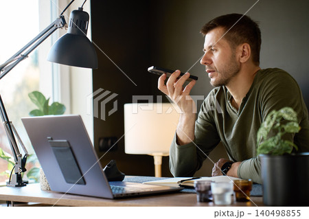 Man using smartphone voice assistant while sitting at home desk Man using smartphone voice assistant while sitting at home desk 140498855
