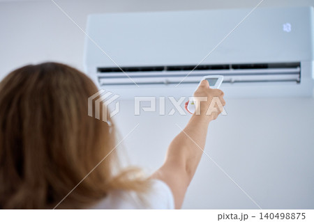 Woman using air conditioner remote control Woman using air conditioner remote control 140498875