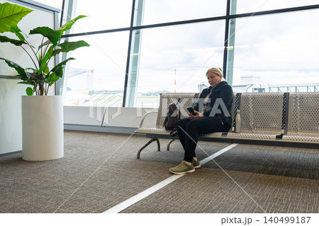 Woman Sitting in Airport Waiting Area Before Flight Departure Checking Her Phone Woman Sitting in Airport Waiting Area Before Flight Departure Checking Her Phone 140499187