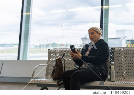 Woman Sitting in Airport Waiting Area Before Flight Departure Checking Her Phone Woman Sitting in Airport Waiting Area Before Flight Departure Checking Her Phone 140499205