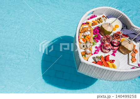 Heart-shaped floating breakfast basket with flowers in a turquoise pool, seen from above. Romantic honeymoon resort indulgence and luxury wellness travel concept for couples. Heart-shaped floating breakfast basket with flowers in a turquoise pool, seen from above. Romantic honeymoon resort indulgence and luxury wellness travel concept for couples. 140499258