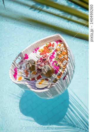 Floating breakfast tray in a turquoise resort pool framed by palm leaves, viewed from above. Tropical luxury hotel lifestyle, honeymoon indulgence and quiet-luxury travel concept with copy space. Floating breakfast tray in a turquoise resort pool framed by palm leaves, viewed from above. Tropical luxury hotel lifestyle, honeymoon indulgence and quiet-luxury travel concept with copy space. 140499260