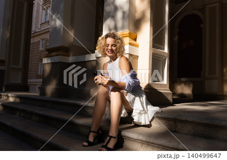 Person sitting on steps, smiling while using smartphone Person sitting on steps, smiling while using smartphone 140499647