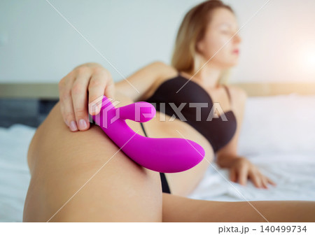 Young sexy woman lying on the bed holding in her hands a sex toy for adults Young sexy woman lying on the bed holding in her hands a sex toy for adults 140499734