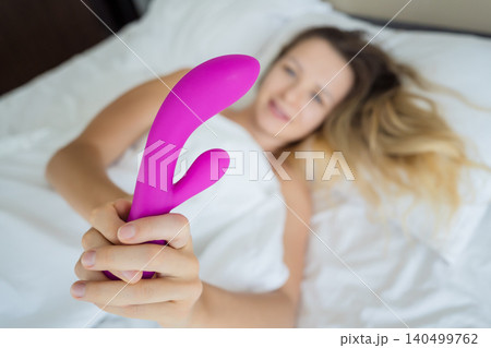 Young sexy woman in the bed holding in her hands a sex toy for adults Young sexy woman in the bed holding in her hands a sex toy for adults 140499762