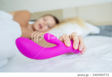 Young sexy woman in the bed holding in her hands a sex toy for adults Young sexy woman in the bed holding in her hands a sex toy for adults 140499772