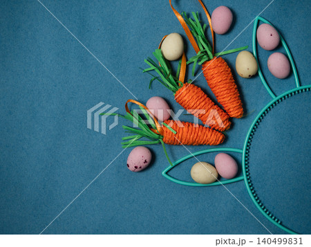 Easter display with bunny rabbit ears eggs and carrots blue background Easter display with bunny rabbit ears eggs and carrots blue background 140499831
