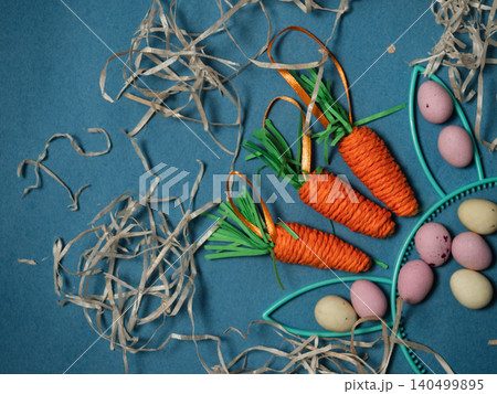 Easter display with bunny rabbit ears eggs and carrots blue background Easter display with bunny rabbit ears eggs and carrots blue background 140499895