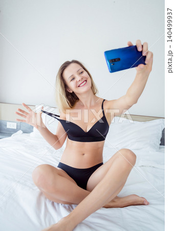 Young sexy woman posing in front of smartphone in his hand and working as webcam model Young sexy woman posing in front of smartphone in his hand and working as webcam model 140499937