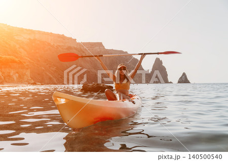 Kayaking Woman Ocean Coastline - Happy woman kayaking in the ocean near a rocky coastline during a summer day. 140500540