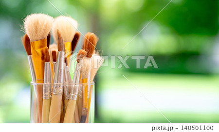 Set of various artist paintbrush in glass holder against a blurry green background of garden 140501100
