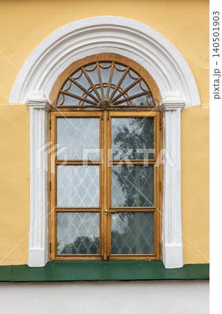 Arched wooden window set in a warm yellow stucco facade 140501903