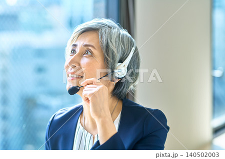 ヘッドセットを手に窓辺で見上げて微笑むグレーヘアの女性 ヘッドセットを手に窓辺で見上げて微笑むグレーヘアの女性 140502003
