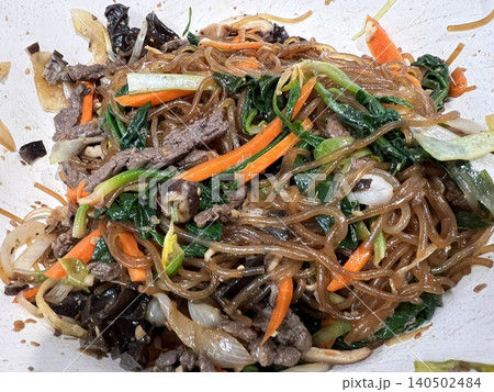 A vibrant plate of japchae featuring stir-fried glass noodles, colorful vegetables, and tender slices of meat, all coated in a savory-sweet soy-based sauce. A classic Korean favorite! A vibrant plate of japchae featuring stir-fried glass noodles, colorful vegetables, and tender slices of meat, all coated in a savory-sweet soy-based sauce. A classic Korean favorite! 140502484