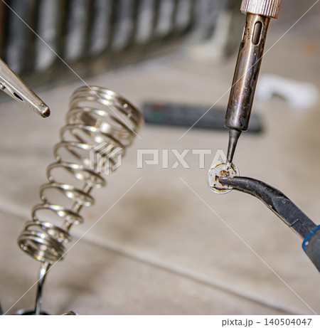 Soldering iron joining wire to metal contact on workbench during electronics repair Soldering iron joining wire to metal contact on workbench during electronics repair 140504047