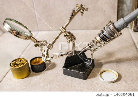 Soldering iron in stand with helping hands magnifier and solder on workbench for electronics repair 140504061