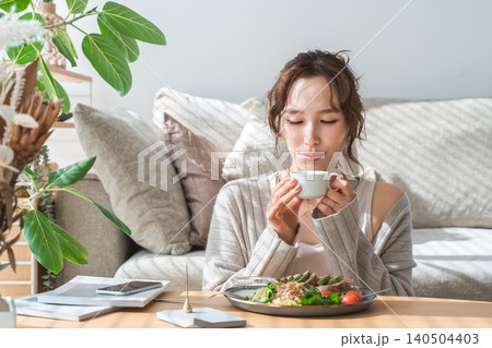 リビングテーブルで食事をするおしゃれな若いアジア人女性 リビングテーブルで食事をするおしゃれな若いアジア人女性 140504403
