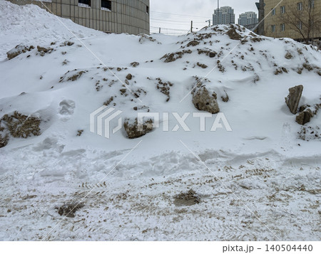 A Winter Landscape Featuring a Snow-Covered Terrain with Boulders and Urban Background, Capturing the Essence of Cold Climates and Seasonal Change 140504440