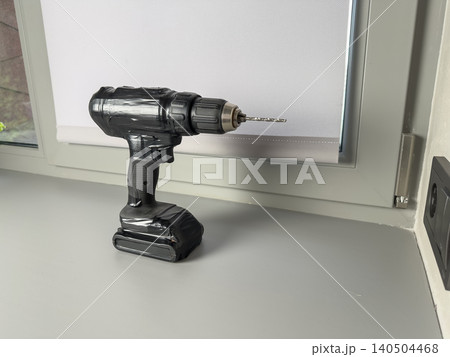 A Close-Up View of a Modern Cordless Drill Positioned on a Clean Work Surface Near a Window, Highlighting Its Functional Design and Quality Craftsmanship 140504468