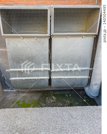 Exploring a Series of Damp Metal Grates Overlooking a Stagnant Green Pool Surrounded by Urban Walls and Infrastructure 140504495