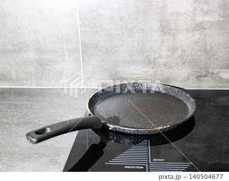 Induction cooktop heating nonstick frying pan with steam in modern kitchen Induction cooktop heating nonstick frying pan with steam in modern kitchen 140504677