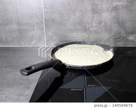 Pan cooking crepe batter on induction cooktop with steam in home kitchen 140504678