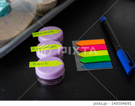 Labeled seed jars for watermelon, cucumber and basil on desk with pen and color page markers 140504691