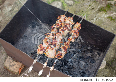 Grilling traditional pork kebab on a metal brazier in the backyard. Summer barbecue weekend with family Grilling traditional pork kebab on a metal brazier in the backyard. Summer barbecue weekend with family 140504902