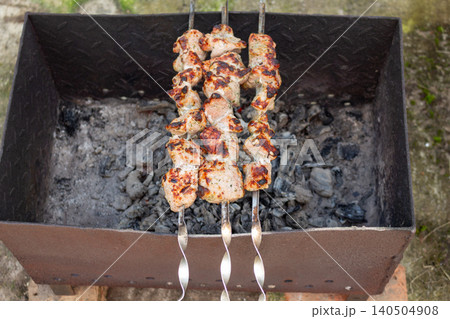 Juicy pork shashlik grilling on skewers over hot charcoal in mangal. Traditional outdoor barbecue picnic Juicy pork shashlik grilling on skewers over hot charcoal in mangal. Traditional outdoor barbecue picnic 140504908