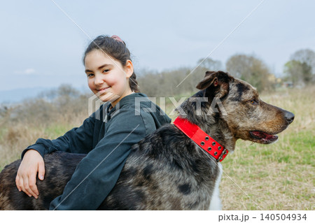 smiling Girl in blue hoodie sits next to her dog outdoors and looking at camera 140504934