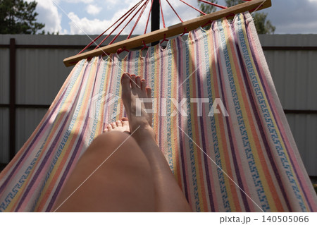 Personal perspective of feet lying in a colorful striped hammock in the backyard. Summer relaxation concept Personal perspective of feet lying in a colorful striped hammock in the backyard. Summer relaxation concept 140505066