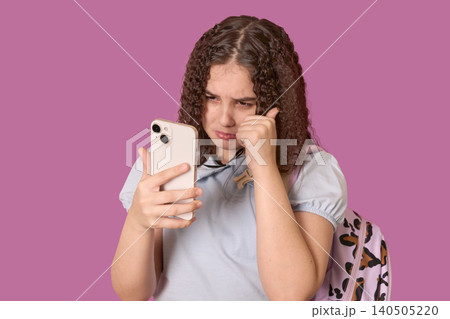 Teenage Girl Expressing Emotions While Looking at Her Smartphone Against a Pink Background Teenage Girl Expressing Emotions While Looking at Her Smartphone Against a Pink Background 140505220