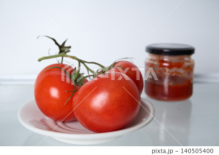 Three red tomatoes on a branch, lying on a white plate on an empty shelf in the refrigerator, next to an incomplete can of tomato paste Three red tomatoes on a branch, lying on a white plate on an empty shelf in the refrigerator, next to an incomplete can of tomato paste 140505400