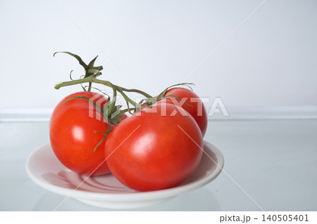 Three red tomatoes on a branch, lying on a white plate on an empty shelf in the fridge Three red tomatoes on a branch, lying on a white plate on an empty shelf in the fridge 140505401